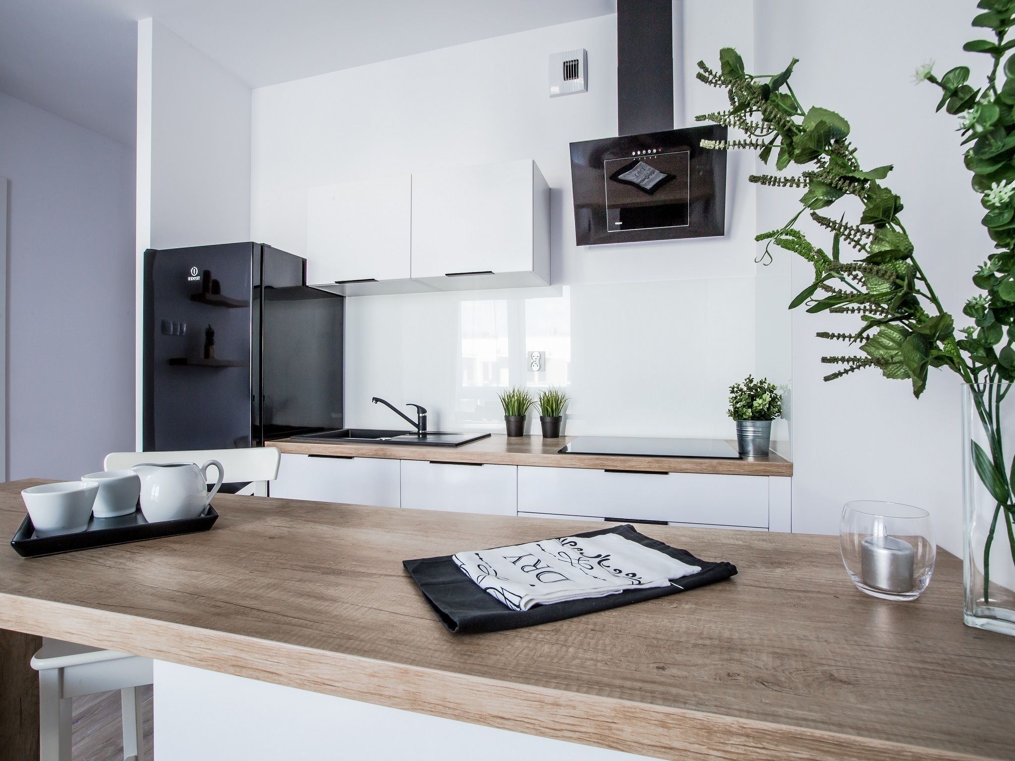 Una cocina moderna con armarios blancos, un refrigerador negro, encimera de madera y una pequeña planta en maceta.