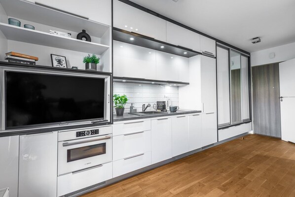 Una cocina moderna con armarios blancos, un horno Bosch, un televisor de pantalla plana grande y una cafetera.