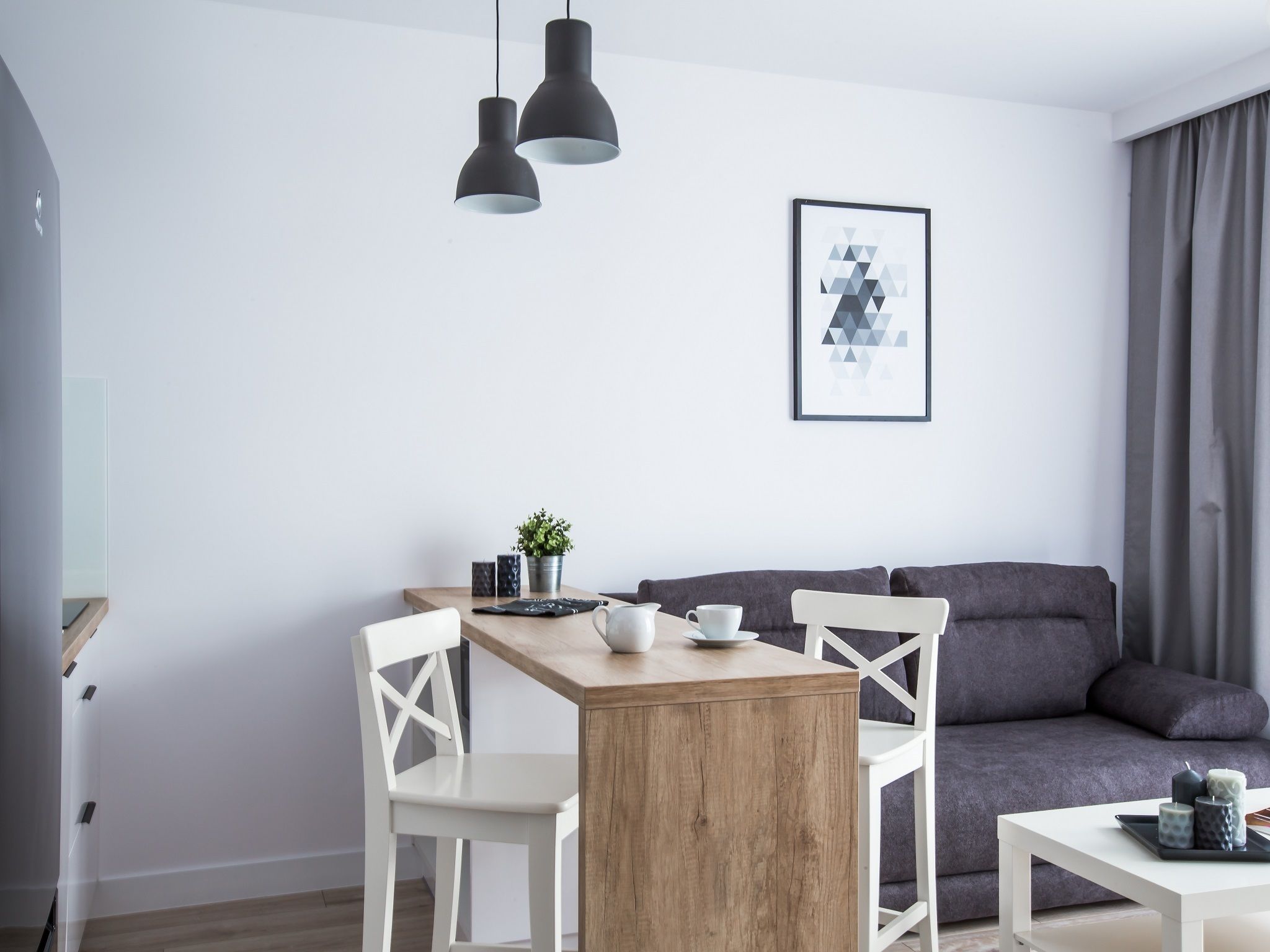A modern living space with a wooden dining table, white chairs, a grey sofa, and a framed abstract artwork on the wall.
