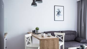 A modern living space with a wooden dining table, white chairs, a grey sofa, and a framed abstract artwork on the wall.