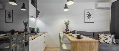 Una cocina moderna con armarios blancos, una mesa de comedor de madera e iluminación colgante.