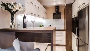 A modern kitchen with white cabinets, a stainless steel refrigerator, and a dining area with a marble countertop and a vase of flowers. - Emihouse CityVibe Apartments (Rzeszów)
