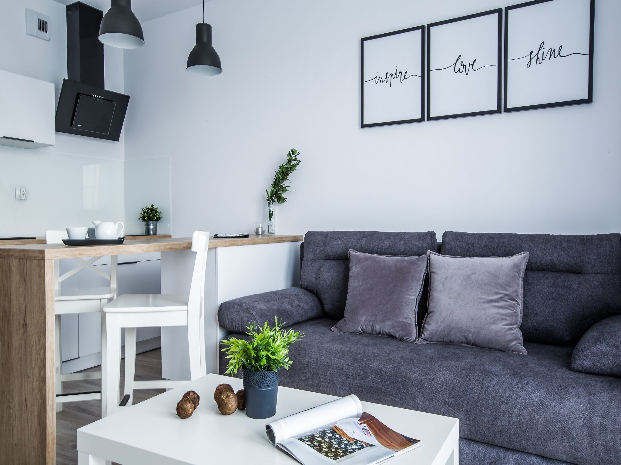 A modern living room with a grey sofa, white coffee table, and a kitchen area with a dining table and chairs.