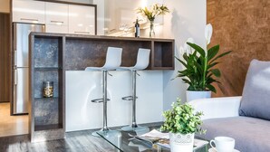 Eine moderne Küche mit Einbaukühlschrank, einer Bar mit Glasplatte und Hockern sowie einer Sitzecke mit Sofa und Couchtisch.
