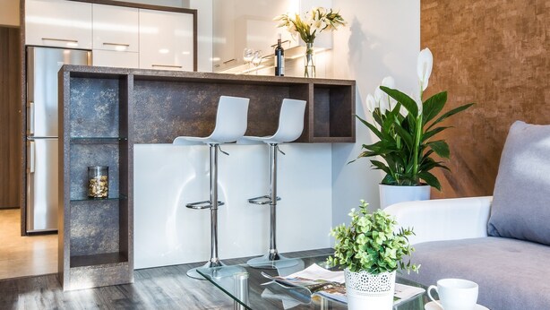 A modern kitchen with a built-in refrigerator, a glass-top bar area with stools, and a seating area with a sofa and a coffee table. - Emihouse CityVibe Apartments (Rzeszów)