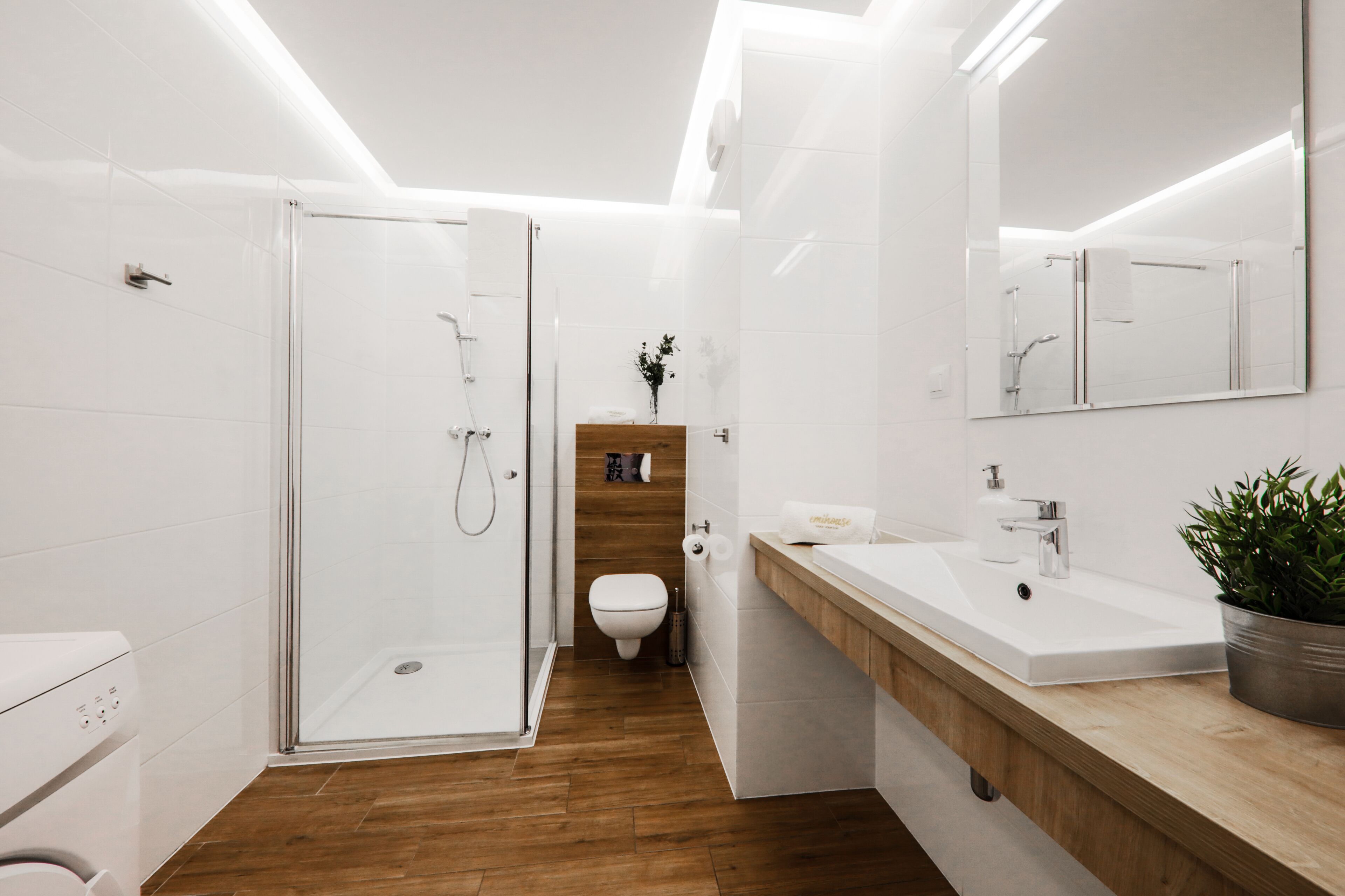 A modern bathroom with a glass shower enclosure, a wooden vanity, a white toilet, and a large mirror.