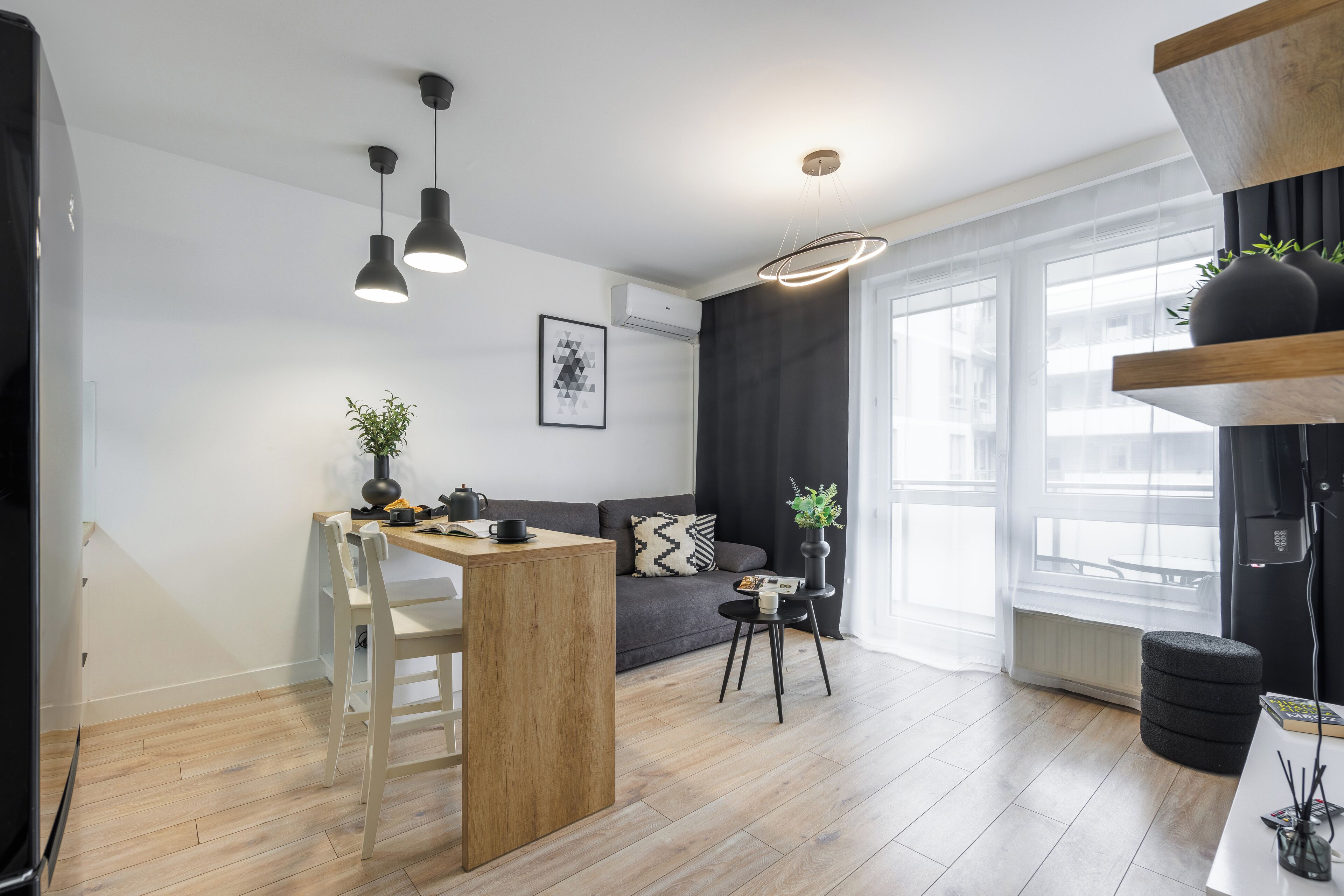 Een moderne keuken met een houten eiland, zwarte hanglampen, een grijze bank en een zwart poef.