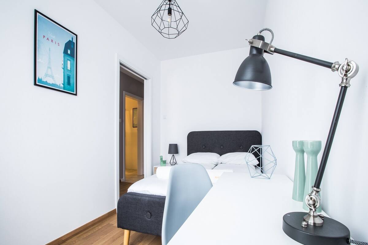 A modern bedroom with a bed, a desk, a lamp, and a picture of the Eiffel Tower on the wall.