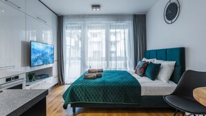 A modern hotel room with a large bed, a flat-screen TV, a desk, and a dining area. - Emihouse CityVibe Apartments (Rzeszów)