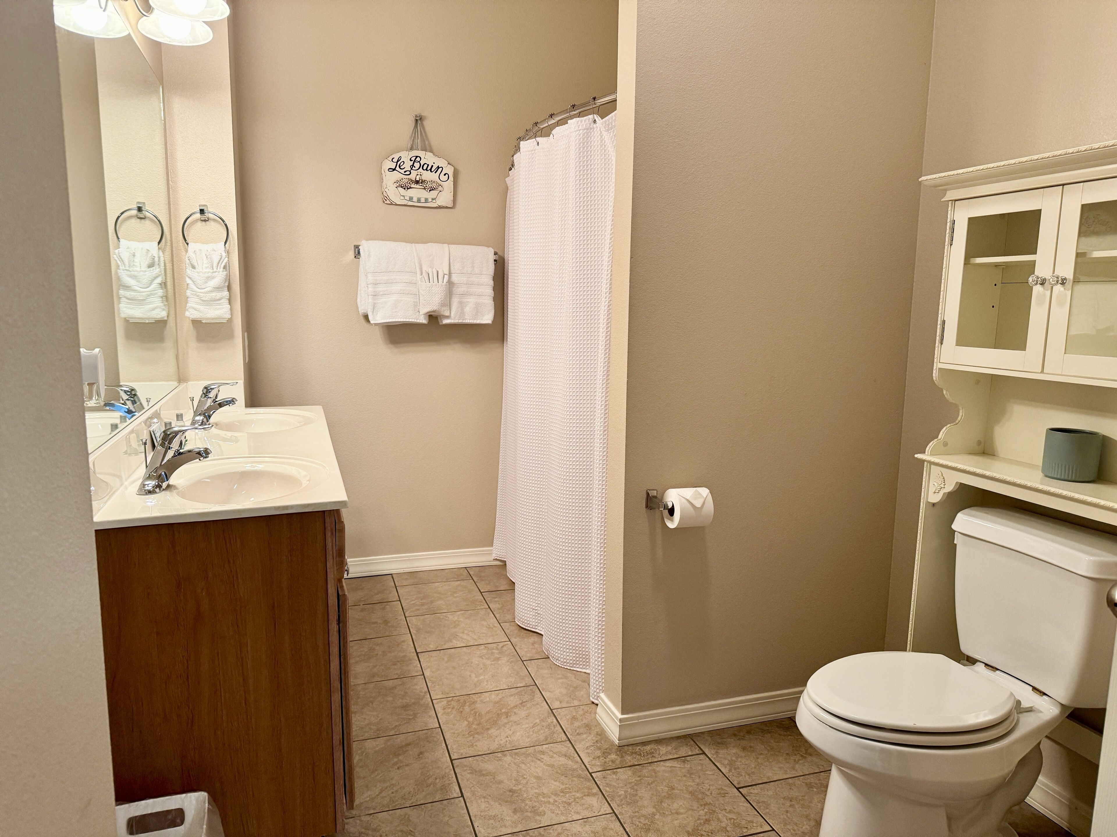 A bathroom with a sink, mirror, towel rack, shower curtain, toilet, and cabinet.