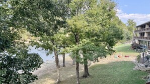 A grassy area with trees, a small body of water, and a building with a balcony. - Walk-in Condo A-4 with Overlooking Deck by RedAwning (Hollister)
