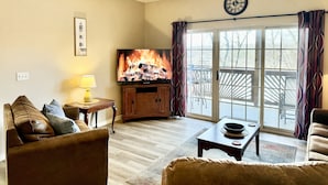 A living room with a fireplace, a ceiling fan, a television, and a view through a glass door. - Walk-in Condo A-4 with Overlooking Deck by RedAwning (Hollister)