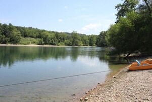 Un lago tranquilo con un bote en la orilla y una colina boscosa al fondo.