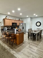 Una cocina moderna con armarios de madera, una isla central con taburetes de bar, una mesa de comedor con sillas y un refrigerador.