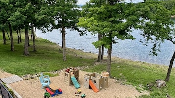 A lakeside park with a playground, a small bridge, and a grassy area with geese.