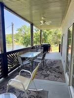 Un patio exterior con zona de estar cubierta, una parrilla y vistas a un lago y árboles.
