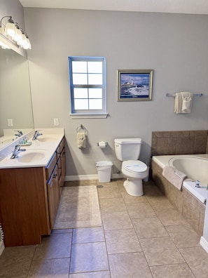 Ein Badezimmer mit Doppelwaschbecken, Toilette, Badewanne und einem Fenster mit Meerblick.
