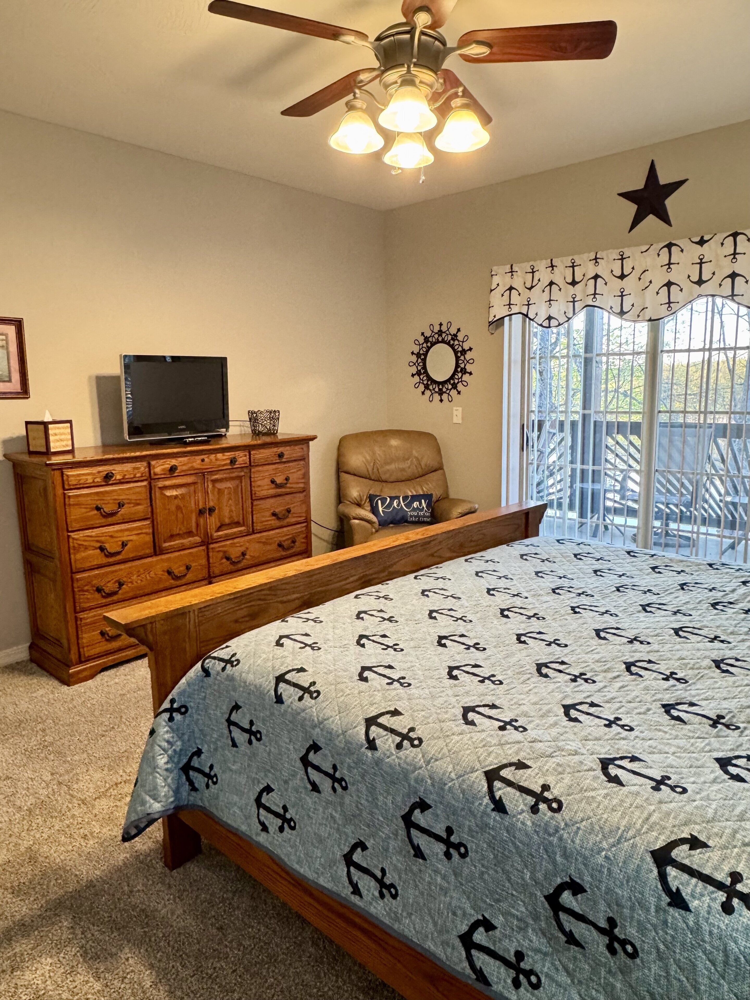 Een slaapkamer met een bed, een houten dressoir, een televisie, een plafondventilator en decoratieve wandelementen.