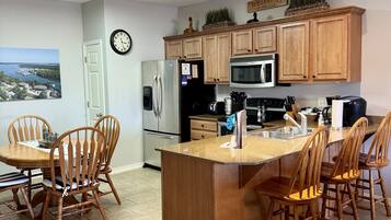 A modern kitchen with wooden cabinets, a stainless steel refrigerator, a microwave, and a dining area with wooden chairs.
