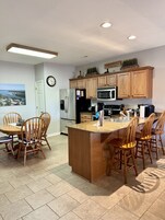 Una cocina moderna con armarios de madera, un refrigerador de acero inoxidable, un microondas y un comedor con sillas de madera.