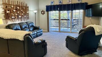 A living room with a ceiling fan, a wall-mounted TV, a decorative fish wall, and a view through a glass door.