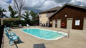 Un área de piscina con terraza de madera, sillas de descanso y un edificio con un letrero que indica las normas de la piscina.