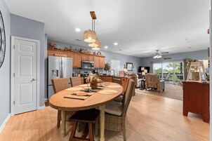 Una cocina moderna con comedor, que incluye una amplia mesa de madera, sillas de mimbre y una lámpara colgante.