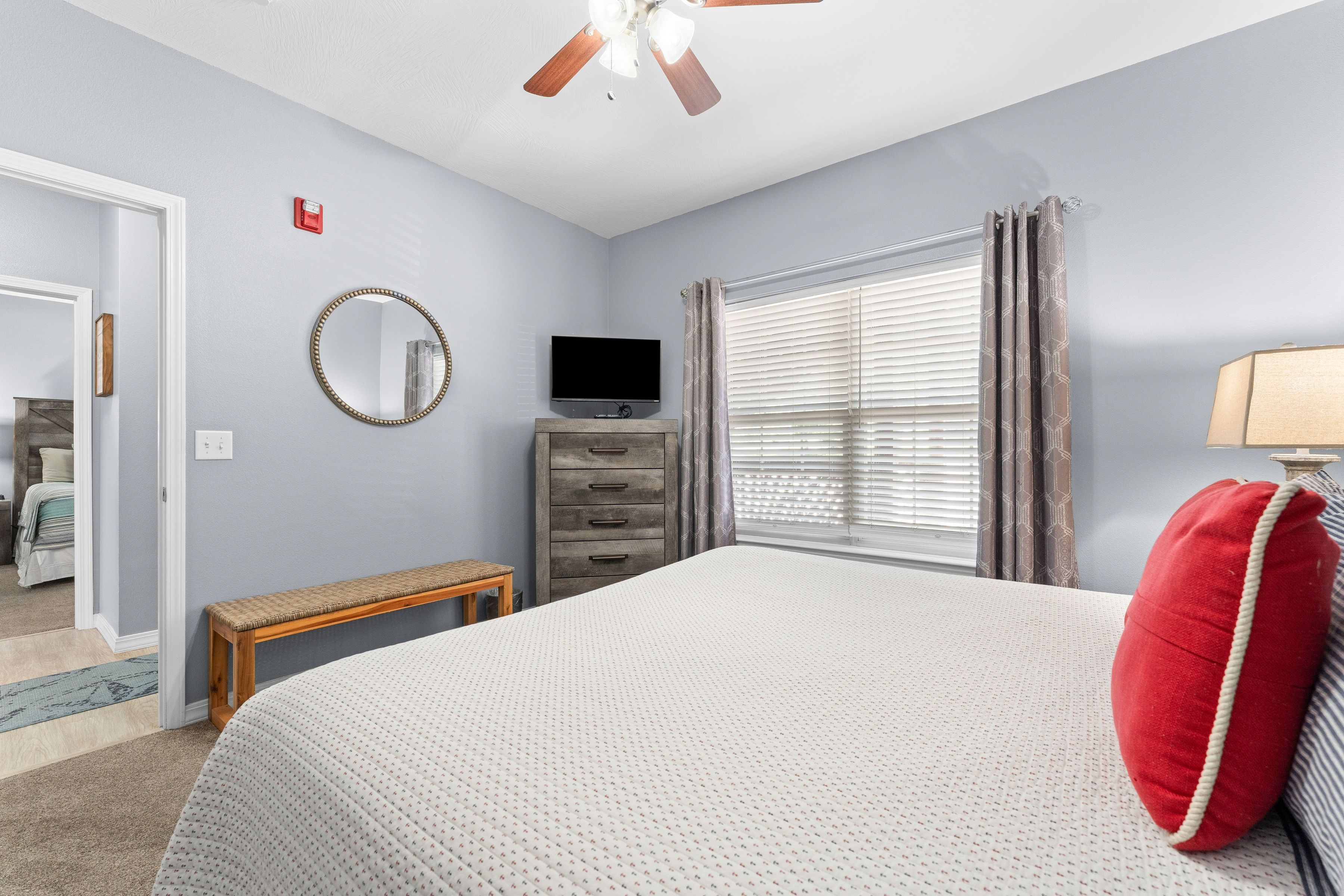A bedroom with a bed, a dresser, a television, a mirror, and a window with blinds.