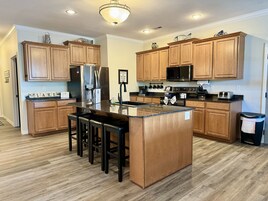 Una cocina moderna con armarios de madera, electrodomésticos de acero inoxidable y una isla central con taburetes de bar.