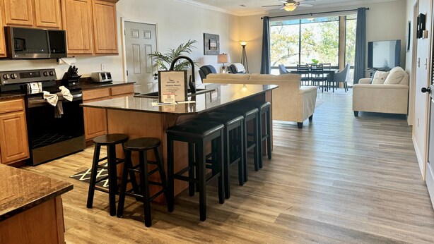 A modern kitchen with wooden cabinets, a central island with stools, a microwave, and a stove.