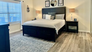 A bedroom with a dark wooden bed, two bedside tables with lamps, a ceiling fan, and nautical-themed wall decor.