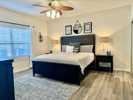 Un dormitorio con una cama de madera oscura, dos mesitas de noche con lámparas, un ventilador de techo y decoración de paredes con temática náutica.