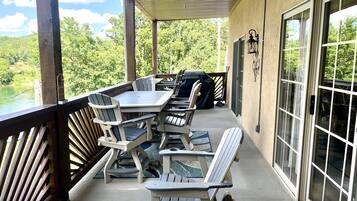 A covered patio with a table and chairs, a grill, and a view of a lake.