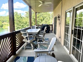 Un patio cubierto con mesa y sillas, una parrilla y vistas a un lago.