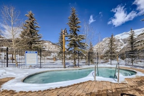 A spa pool surrounded by snow-covered trees and mountains, with a sign detailing spa rules. - Copper Springs 132 (Copper Mountain)