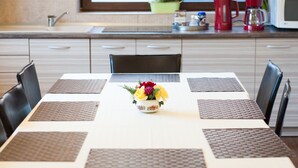 A dining table with four chairs, a vase with flowers, and a kitchen in the background. - Vila Alma (Baile Felix)
