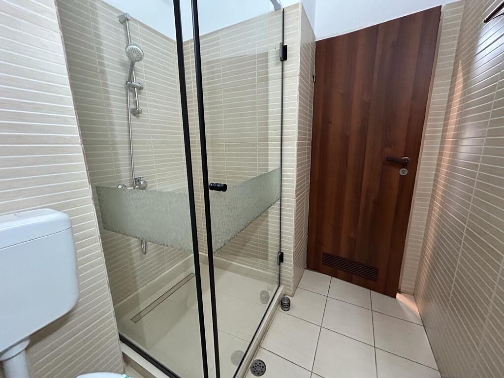 Ein modernes Badezimmer mit Duschkabine aus Glas, einer Holztür und gefliesten Wänden.