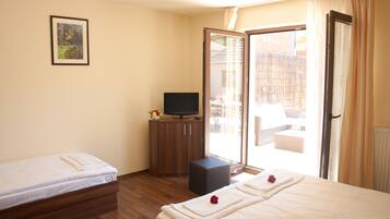 A hotel room with a bed, a TV on a wooden cabinet, a small stool, and a sliding glass door to the outside.