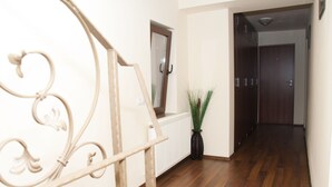 A hallway with wooden flooring, a radiator, a potted plant, and a door at the end. - Vila Alma (Baile Felix)