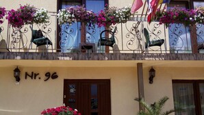 A hotel facade with balconies adorned with flower boxes and flags, a wooden door, and a sign reading "Nr. 96". - Vila Alma (Baile Felix)