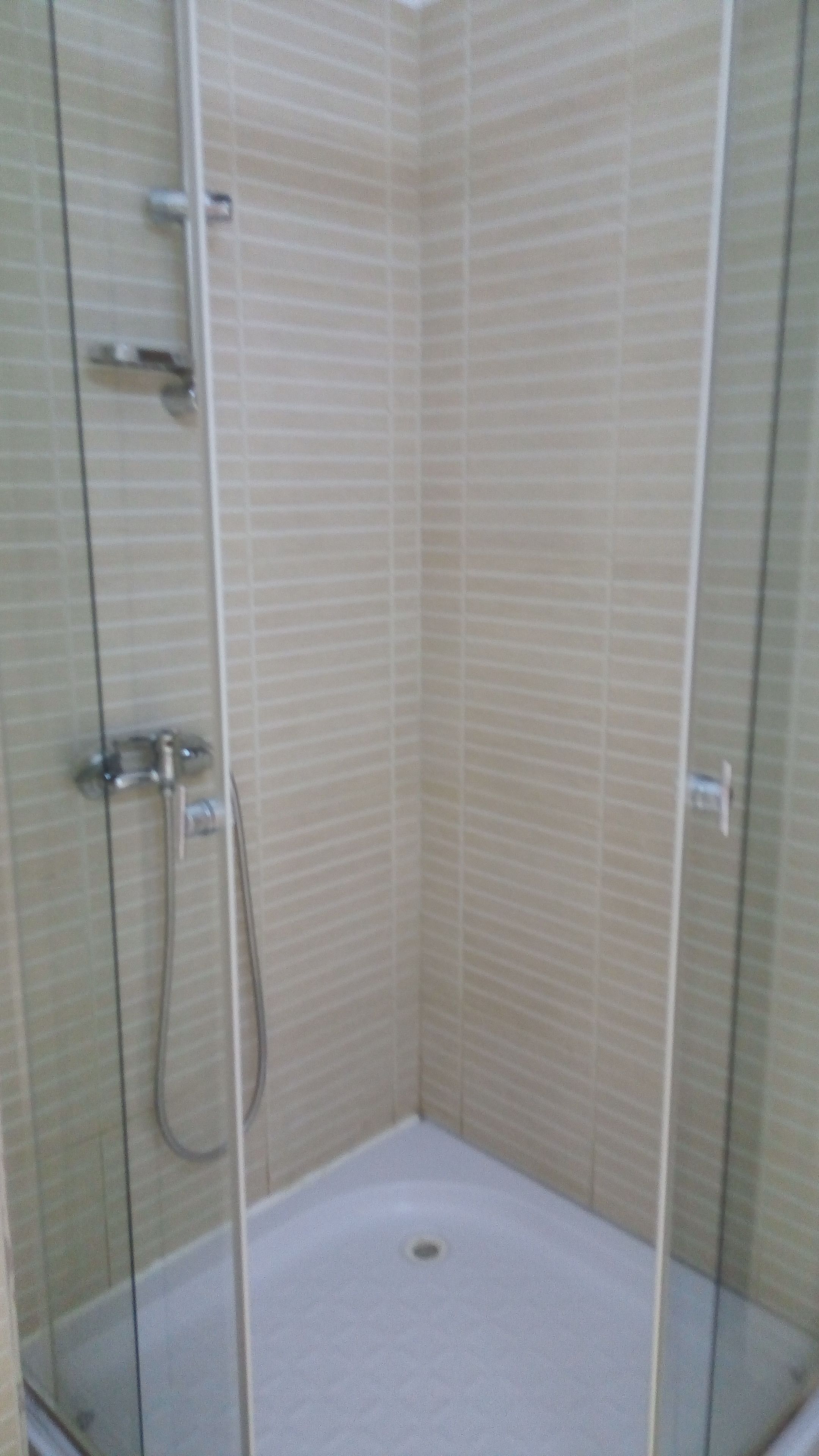 A corner shower with a glass door, a handheld showerhead, and a wall-mounted faucet.