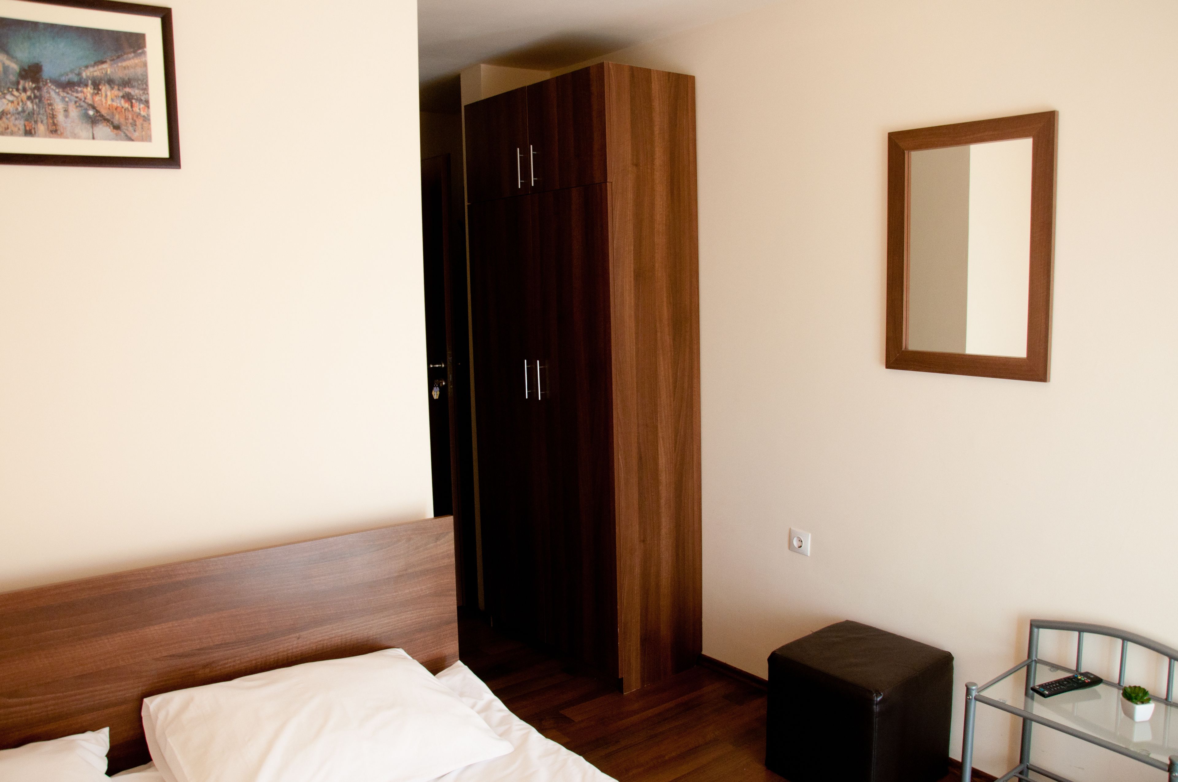 A bedroom with a wooden bed, a wardrobe, a small table with a plant, and a mirror on the wall.
