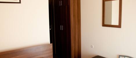 A bedroom with a wooden bed, a wardrobe, a small table with a plant, and a mirror on the wall.