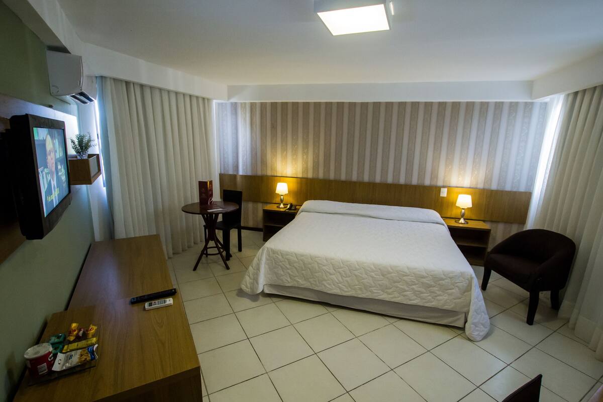 Una habitación de hotel con una cama grande, dos mesitas de noche con lámparas, un escritorio con silla y un televisor montado en la pared.