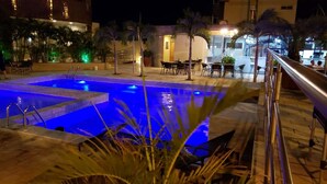 A nighttime pool area with a blue-lit pool, outdoor seating, and palm trees. - Garbos Trade Hotel (Mossoro)