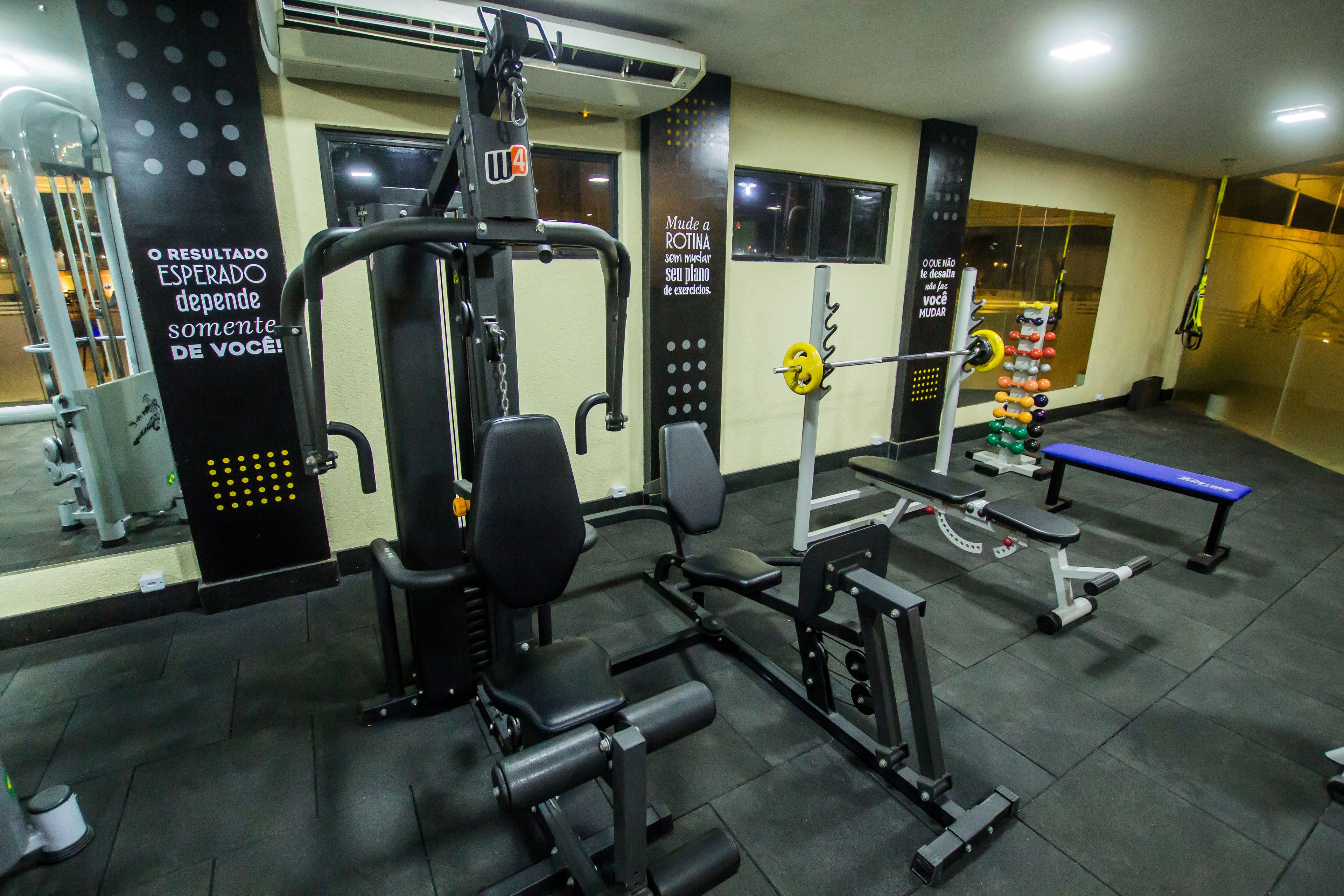 Un gimnasio con equipo de ejercicio, una banca y carteles motivacionales en las paredes.