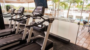 A gym with treadmills, a TV, and a view of a pool and outdoor seating area. - Garbos Trade Hotel (Mossoro)