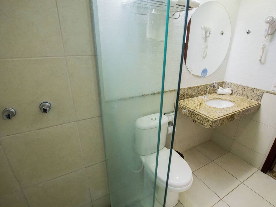 Une salle de bain avec une douche à parois de verre, des toilettes, un lavabo avec une serviette et un miroir avec un téléphone.