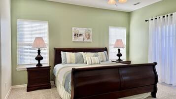 A bedroom with a bed, two bedside tables, a ceiling fan, and two windows with blinds.