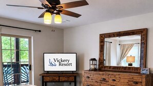 A bedroom with a bed, a dresser, a ceiling fan, a TV, and a door leading to a balcony.